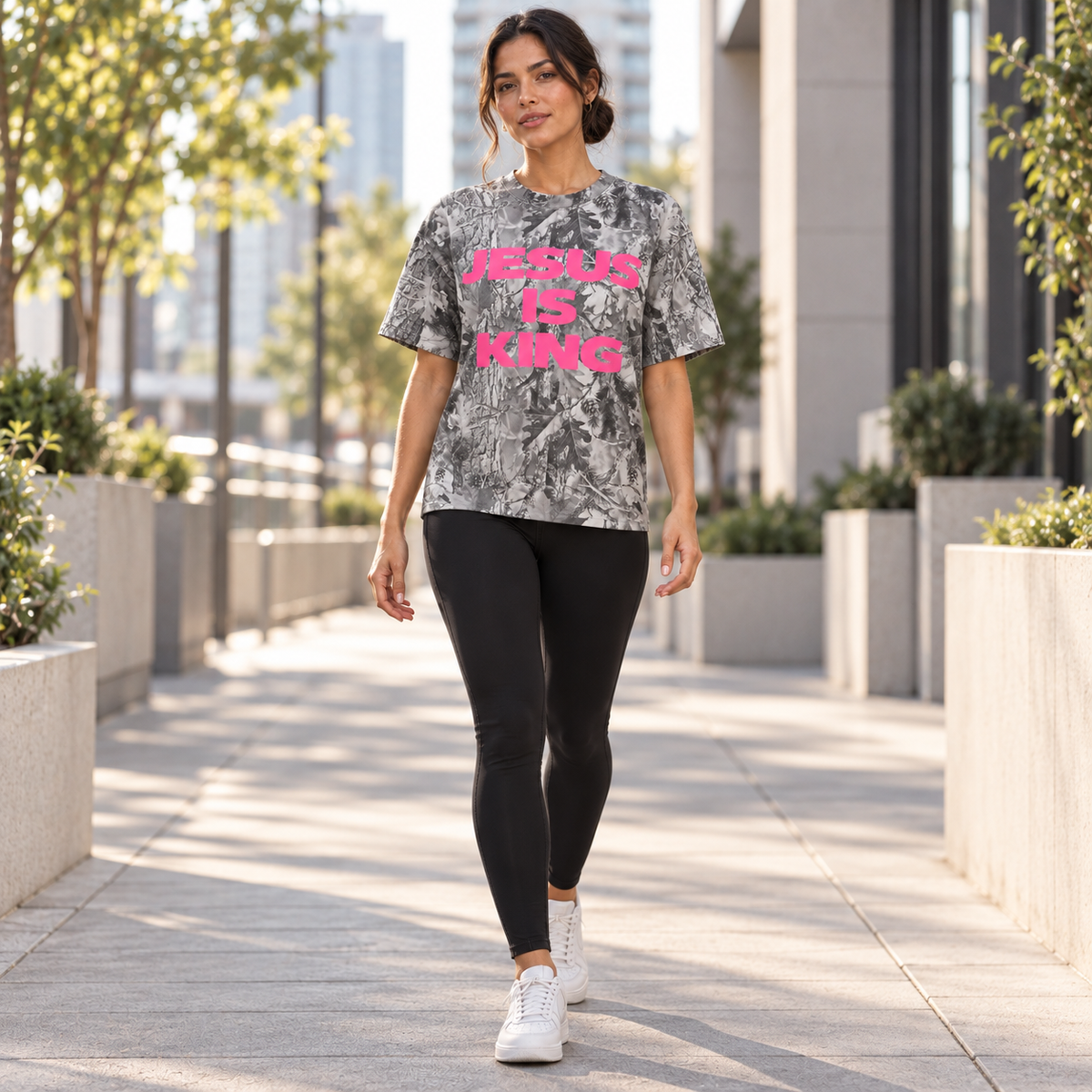 Woman walking outdoors in a JESUS IS KING pink camo tee and black leggings
