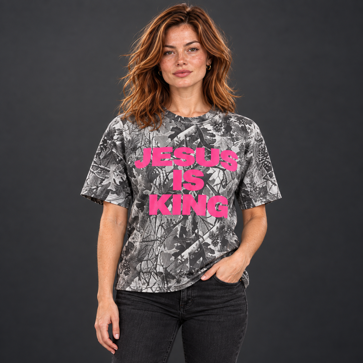 Red-haired woman wearing a JESUS IS KING pink camo tee with her hand in her pocket