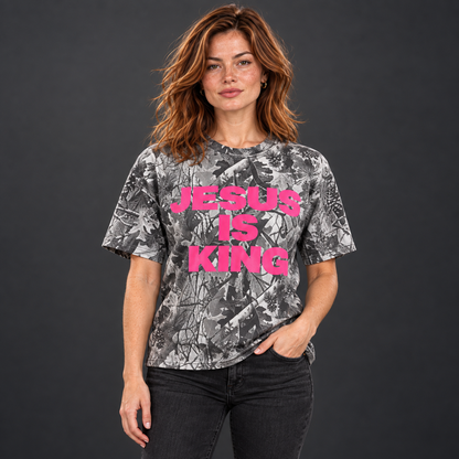 Red-haired woman wearing a JESUS IS KING pink camo tee with her hand in her pocket